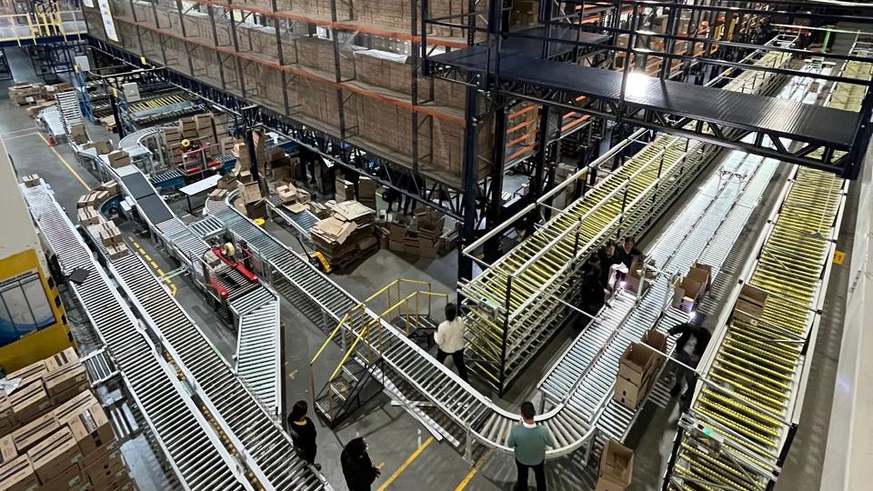 Order-fulfilment floor with roller conveyors, flow-rack picking modules and an elevated walkway, Colombia